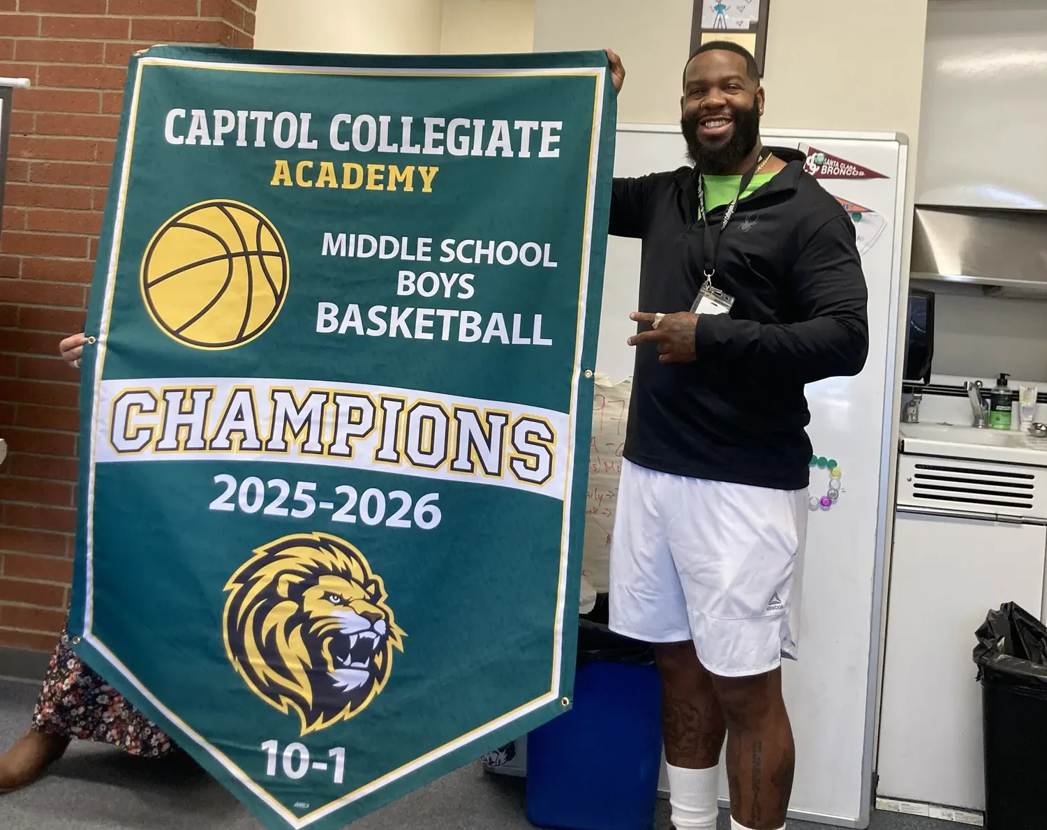 Coach with the Capitol Collegiate middle school boys basketball champions banner, 2025–2026